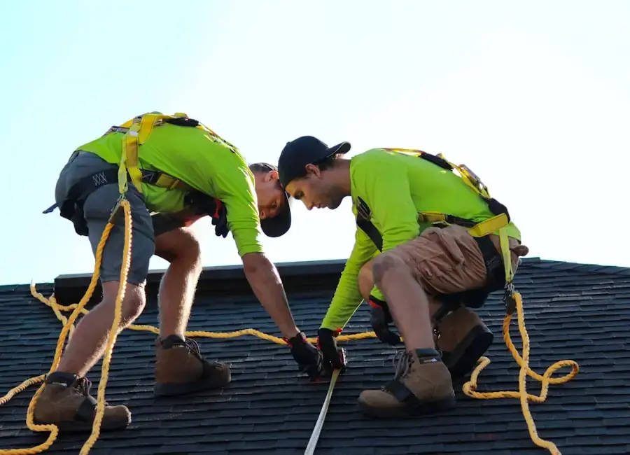 Two roofers in safety harnesses working on a low-slope roof