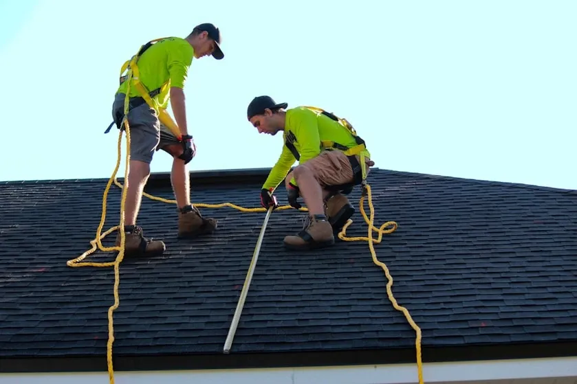 Two roofers measuring a newly shingled roof