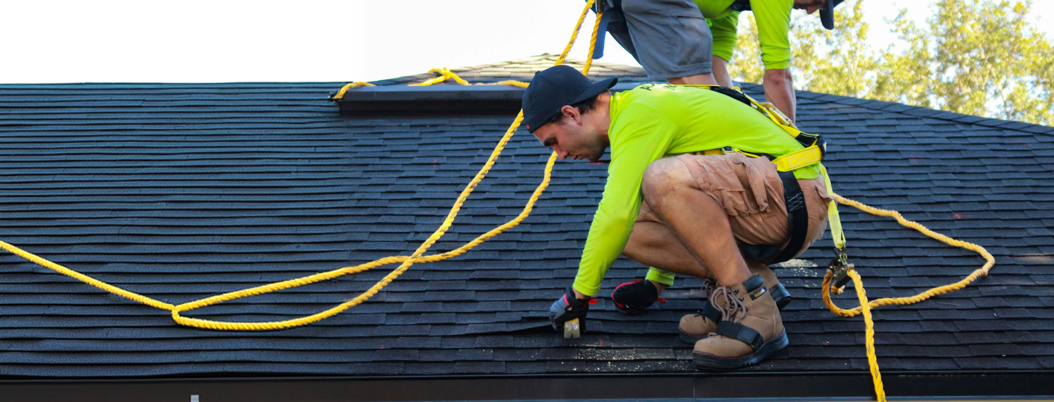 Roofer in a safety harness installing shingles on a residential roof