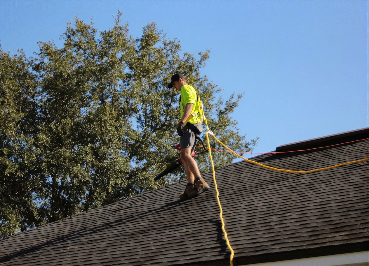 Roofer in a safety harness inspecting a storm-damaged shingle roof