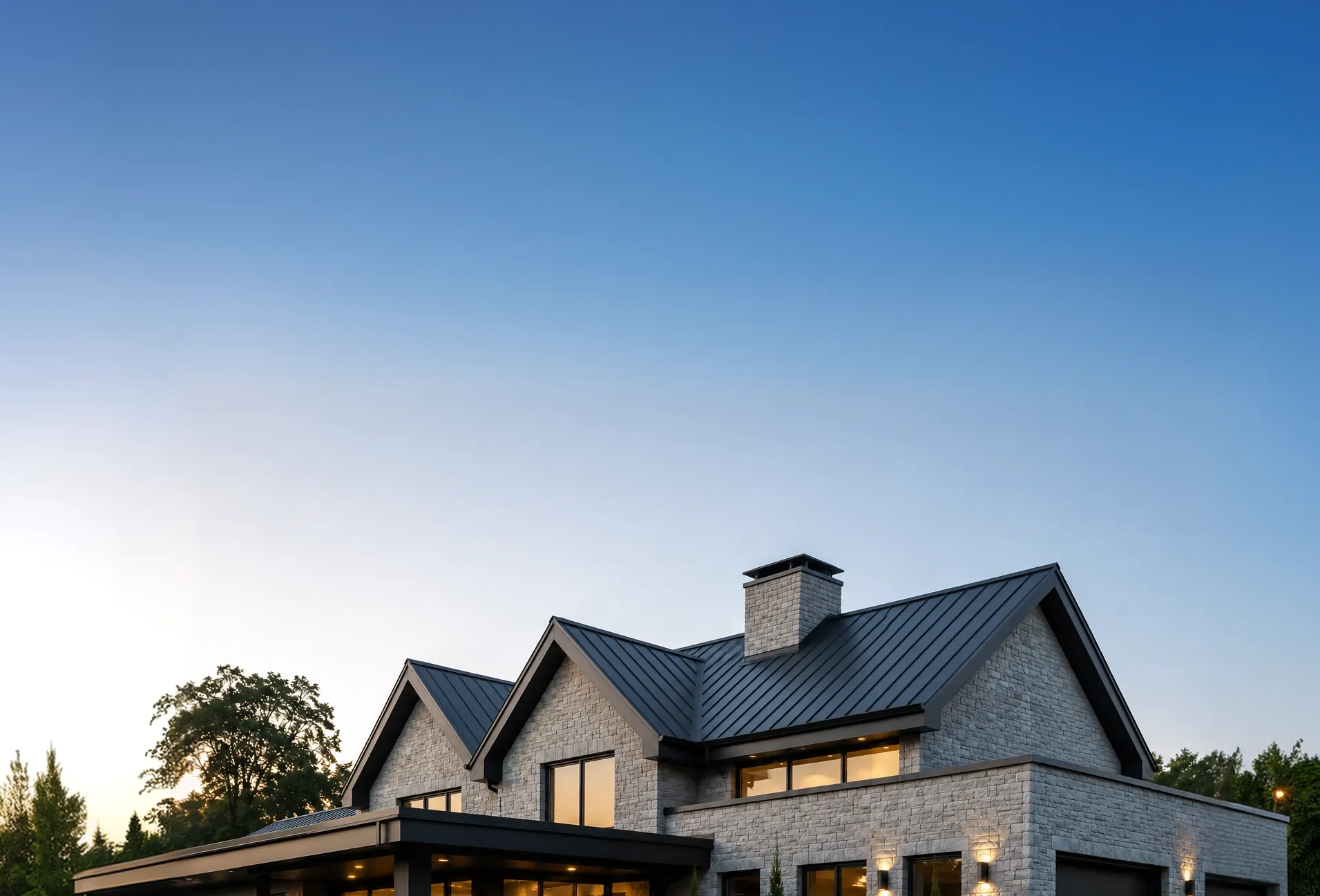 Stone house with a dark standing-seam metal roof against a clear evening sky